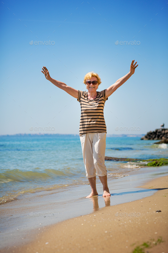 Elderly woman walking along the beach and showing her palm hands covered in sand