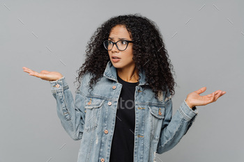 Confused unaware Afro woman with crisp hair, raises hands in bewilderment, looks aside