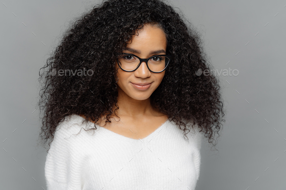 Close up shot of dark skinned female has satisfied expression, bushy curly hair