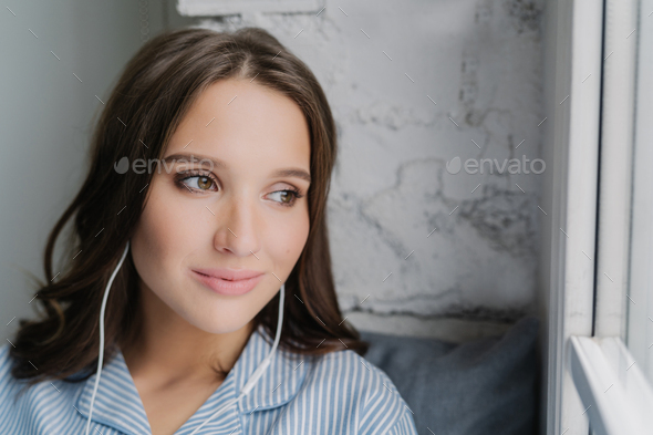 Headshot of attractive female meloman enjoys music in earphones with high volume