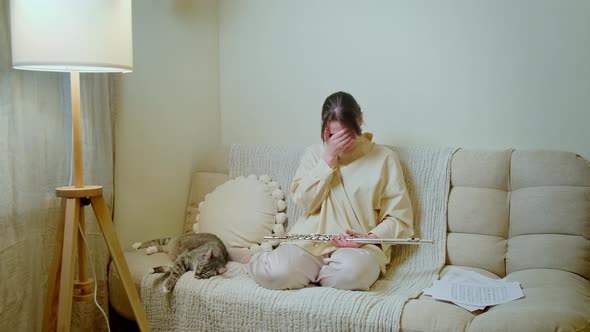 Crying woman with a flute is playing at home on the sofa in the living room