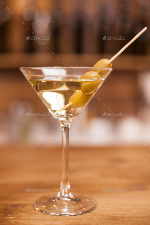 Delicious martini drink with green olives on stick over a wooden bar
