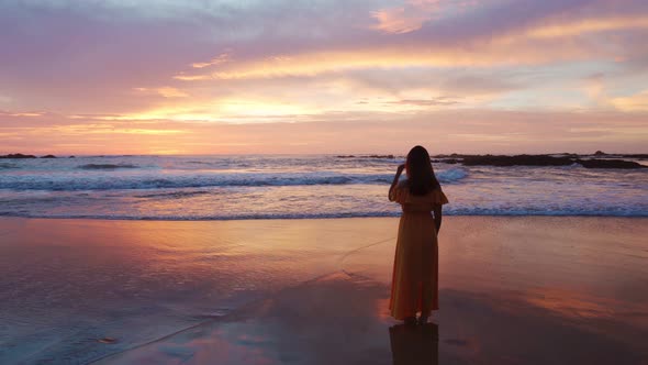 Lonely young asian woman standing on the beach at sunset	