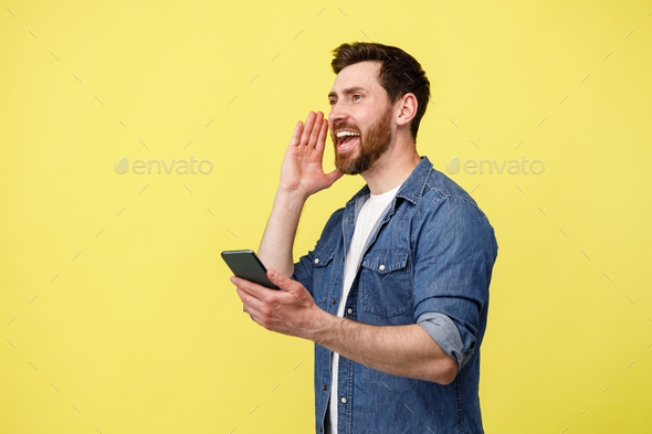 Handsome man loudly calls someone and holds mobile phone in his hands
