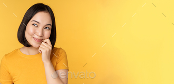 Close up portrait of cute asian girl smiling, thinking, looking up thoughtful, standing in tshirt