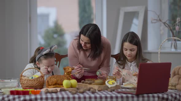 Front View Positive Caucasian Woman and Girls Coloring Eggs on Easter Sunday Watching Online Recipe alt