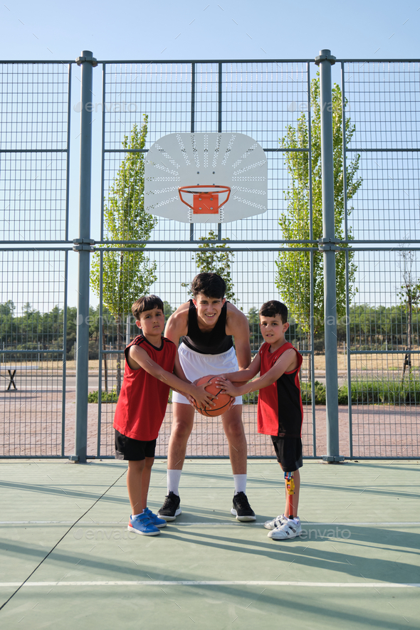 Basket trainer and two students looking at camera with a basketball.