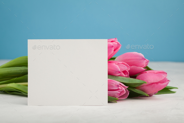Birthday or wedding mockup with white paper list, pink tulip flowers on blue background.