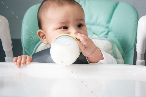 The baby eats from a bottle at the feeding table. Introduction of complementary foods, child care