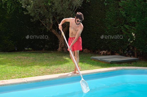 Young man cleaning swimming pool of fall leaves with cleaning net.