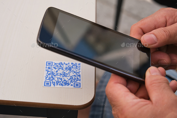 Man hand using the smartphone to scan the QR code in a bar table.