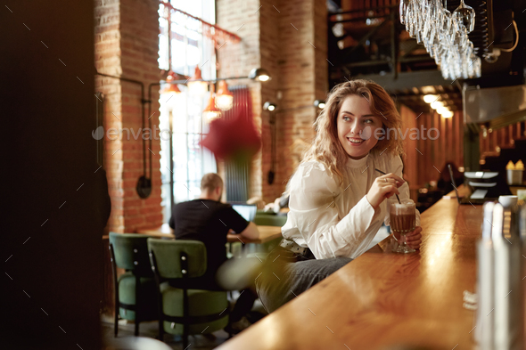 Positive woman sitting at bar counter and drinking coffee