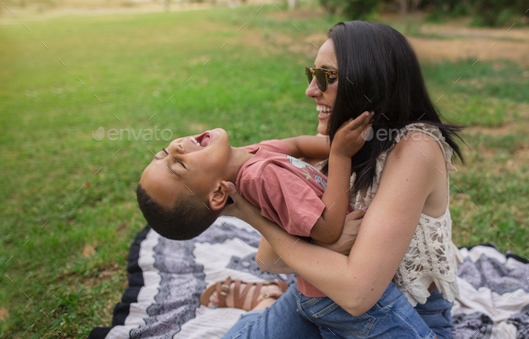 Mother tickling her son, sitting on the grass in a park