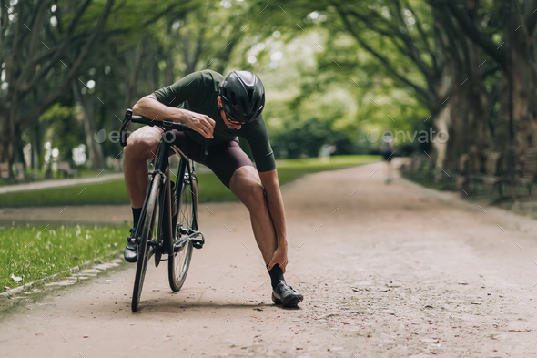 Exhausted sportsman massaging legs after cycling at park