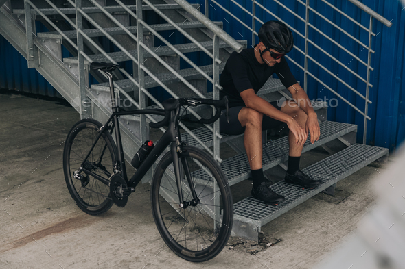 Exhausted cyclist sitting on metal stairs near bike outdoors