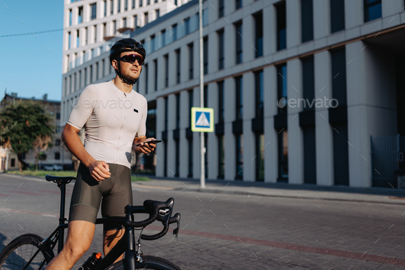 Sportsman holding mobile while standing on street with bike - Stock Photo - Images