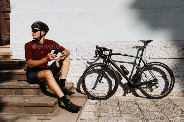 Man in sportswear using mobile while sitting in bike - Stock Photo - Images