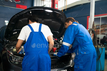 Mechanic in blue overalls checking serviceability of car engine