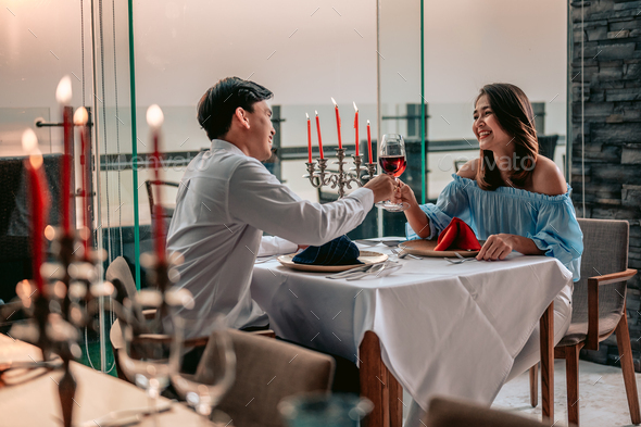 Asian couple with glasses of wine having romantic candlelight dinner in table at restaurant hotel.