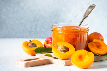 Apricot jam in glass jar at white table.