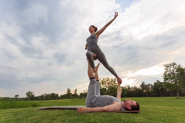 Healthy man lying on grass and balancing woman. Couple doing acrobatic ...