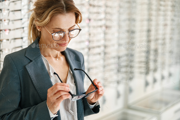 Focused woman inspects a spectacle frame in an optician's shop Stock ...