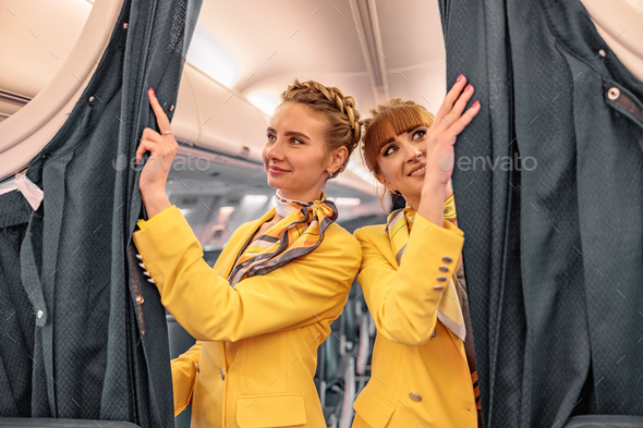 Joyful flight attendants adjusting curtains in airplane