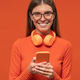Woman with phone and headphones around neck browsing music playlist on orange background - PhotoDune Item for Sale