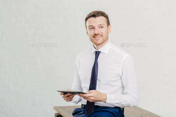 Indoor shot of pleased male owner of prosperous company dressed in formal clothes