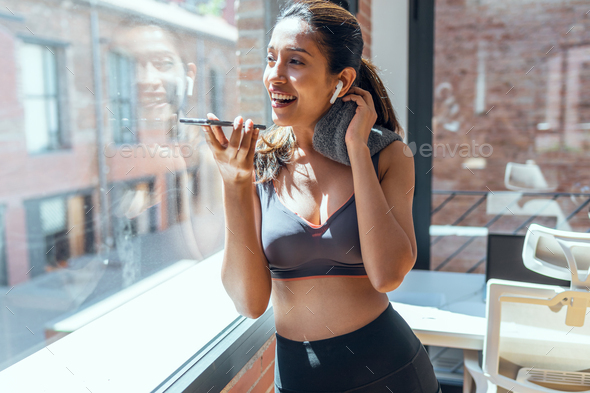 Sporty young woman sending voice message with her smart phone while take a break of exercise at home
