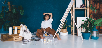 Attractive young female artist sitting  on studio floor with paints enjoying her hobby