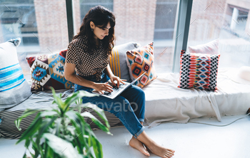 Pretty female freelancer browsing network while working distantly and shopping online with netbook