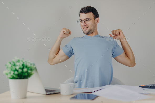 Overworked male freelancer stretches at work place, just finishes with work