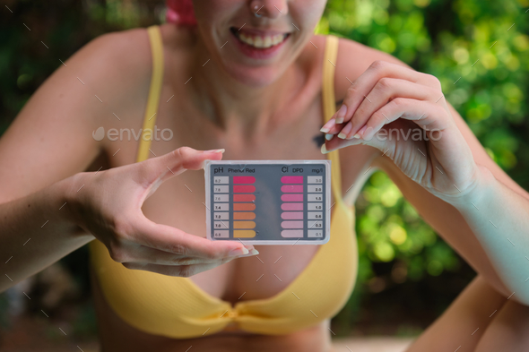 Young caucasian woman using a ph and cl kit to test the pool water quality.