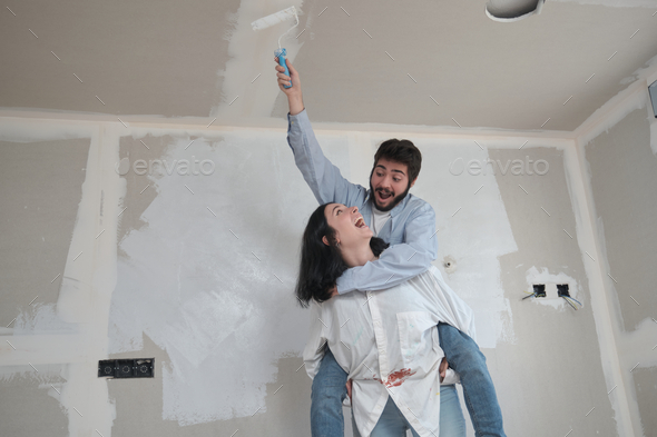 Woman give her friend a piggyback ride to paint the ceiling in their new house.