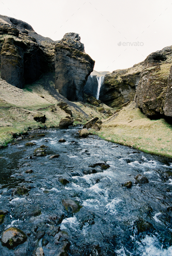 River with rapids flows among the mountains against the backdrop of a waterfall. Iceland