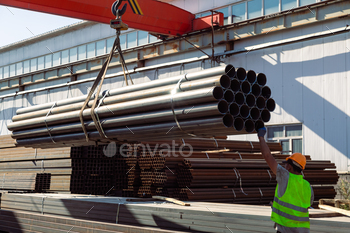 Worker transporting stack of metal pipes with gantry crane