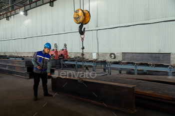 Worker receiving a metal bar from crane in warehouse