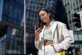Attractive young businesswoman in white suit using phone standing near business centre
