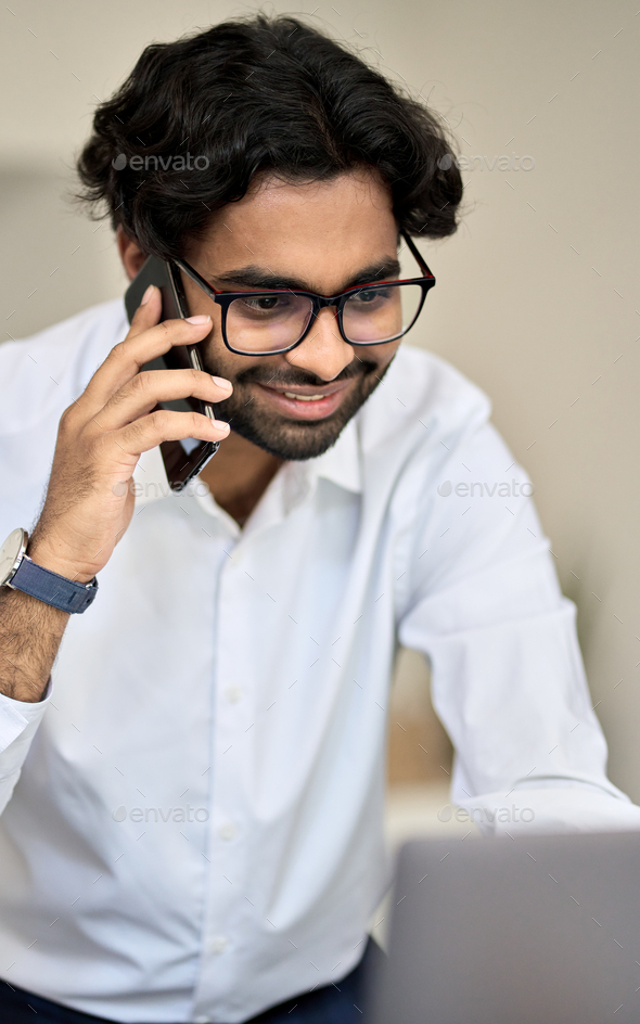 Smiling indian bank manager talking on phone consulting client using pc.