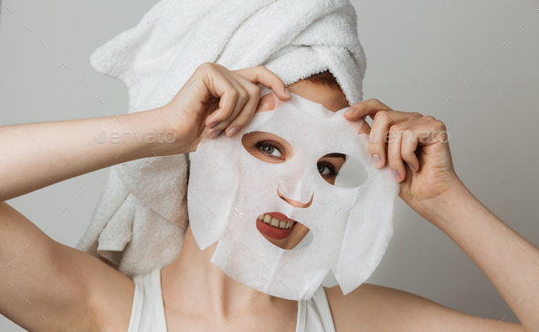 Portrait of beautiful young woman smiling on camera with cotton mask sheet in hands.