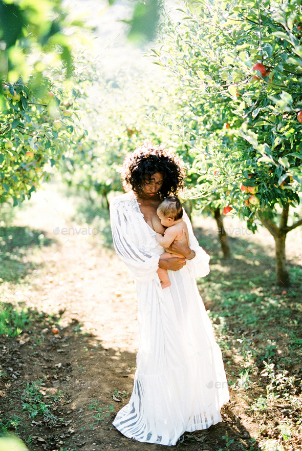 Woman breastfeeding her baby standing under an apple tree in the garden
