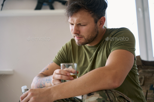 Mentally traumatised soldier drinking alcohol alone at home