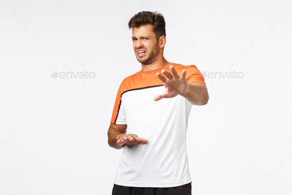 Handsome male athlete in sports t-shirt, step back and grimacing, cringe seeing disgusting thing