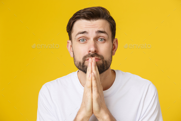 Young guy dressed casually isolated on yellow background, having put hands together in prayer or