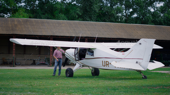 Aviator inspecting small airplane landed on airdrome. Aviator checking plane.