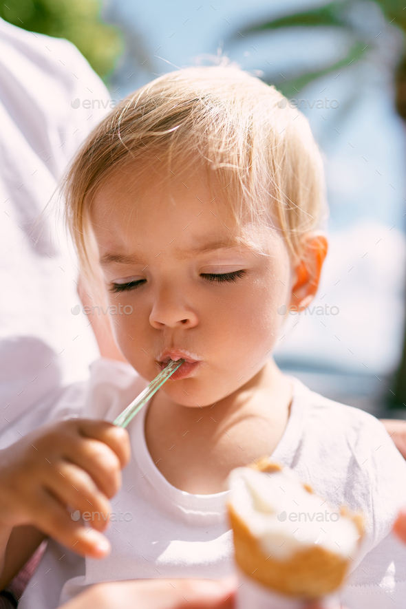 Little girl eating ice cream with a spoon sitting on mom lap
