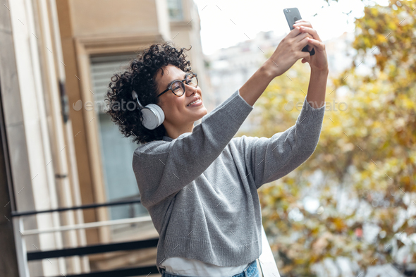 Beautiful woman taking photos with her smartphone while listening to music standing in the balcony