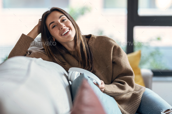 Beautiful woman relaxing while looking at camera on sofa at home. - Stock Photo - Images
