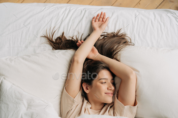 Top view of young beautiful sleepy brunette woman resting in bed after waking up